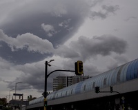 Storm clouds gathering above a cityscape with a pedestrian crossing signal and an elevated metro line