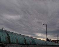 An elevated metro line and a street lamp under swirling cloudy sky